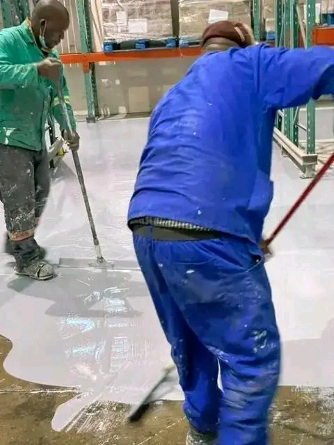 Two workers finishing a large epoxy-coated warehouse floor between pallet racking