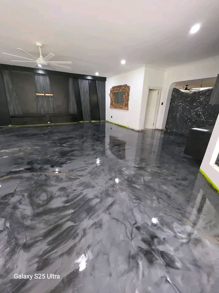 A finished metallic epoxy resin floor in charcoal and silver, reflecting a dark feature wall and ceiling fan